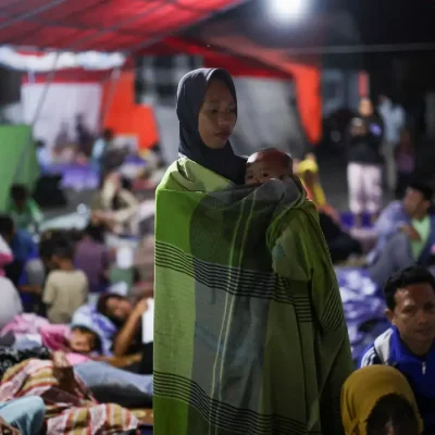 A woman holds a baby as people rest in a shelter at a makeshift evacuation center at a stadium in the aftermath of an earthquake, in Maumere, East Nusa Tenggara, Indonesia, August 16, 2026. REUTERS/Edgar Su/Proibido Reprodução