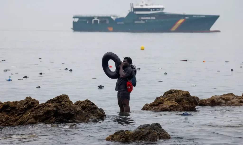 A man holds an inflatable ring, as he stands in the water, with the Spanish Guardia Civil (Civil Guard) in the background, amid mass crossings of migrants on foot and by sea from Morocco into Spanish territory, in Ceuta, Spain, July 31, 2026. REUTERS/Jon Nazca        TPX IMAGES OF THE DAY