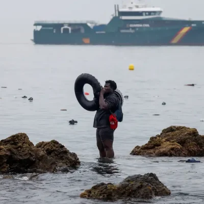 A man holds an inflatable ring, as he stands in the water, with the Spanish Guardia Civil (Civil Guard) in the background, amid mass crossings of migrants on foot and by sea from Morocco into Spanish territory, in Ceuta, Spain, July 31, 2026. REUTERS/Jon Nazca TPX IMAGES OF THE DAY