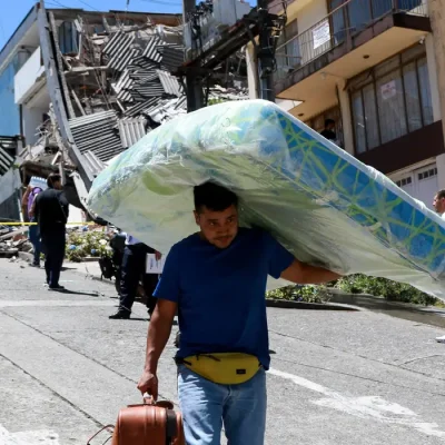 A man carries a mattress down the street in front of damaged buildings after an earthquake, in Manizales, Colombia August 10, 2026. REUTERS/Andres Camilo Valencia/Proibida Reprodução