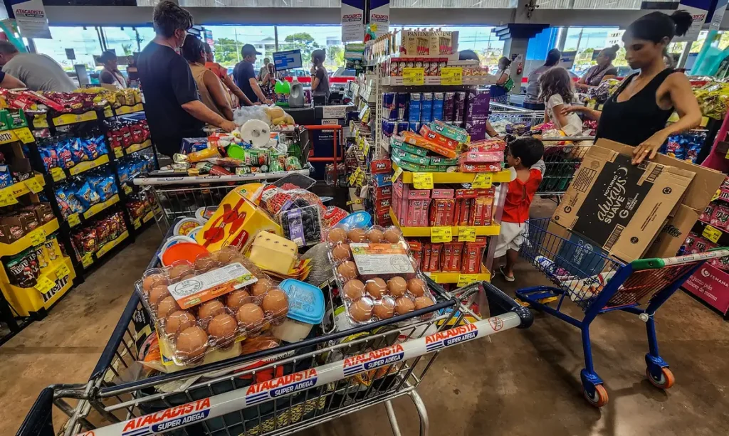 12/06/2026 - Brasília - Consumidores enfrentam longas filas nos caixas de um grande mercado atacadista para finalizar suas compras. Diante do cenário de inflação acumulada e da constante alta de preços nos itens básicos de alimentação, a busca por qualquer tipo de desconto ou promoção tornou-se estratégia essencial para aliviar o orçamento das famílias.Foto: Rafa Neddermeyer/Agência Brasil