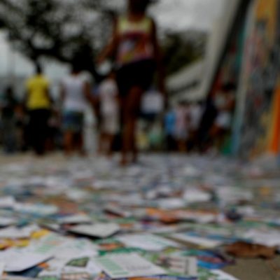 rua urbana com o chão completamente coberto por santinhos e panfletos de campanha eleitoral.